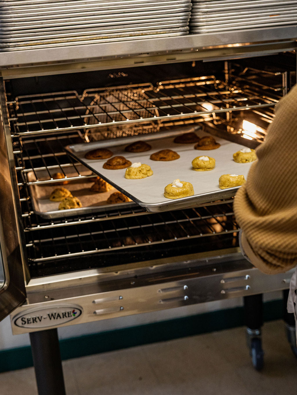 Person placing a tray of cookies into an open industrial oven.