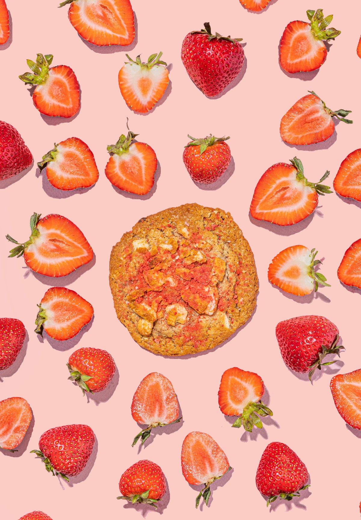 Cookie surrounded by sliced strawberries on a pink background
