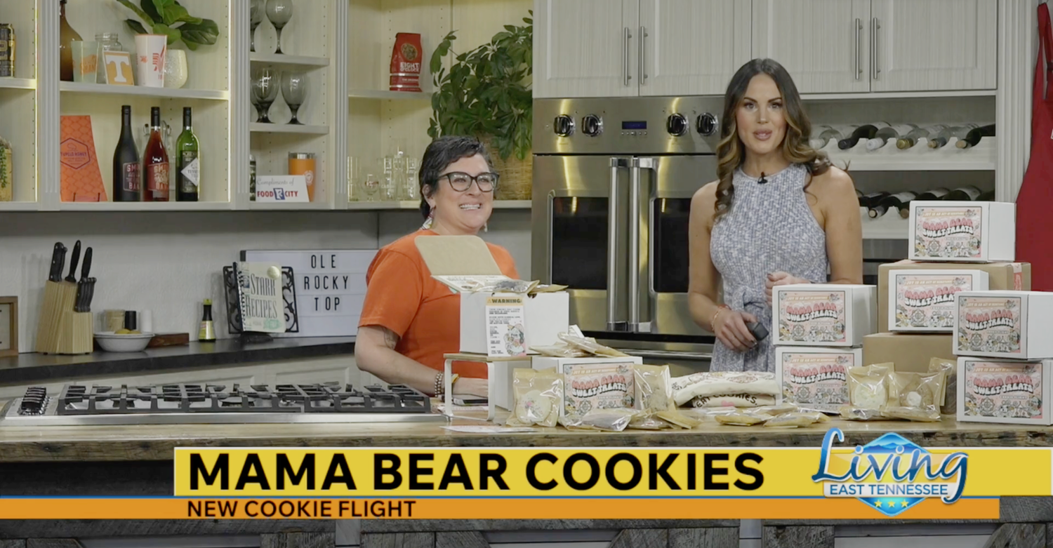 Two women standing behind a counter with 'Mama Bear Cookies' packaging in a kitchen setting.